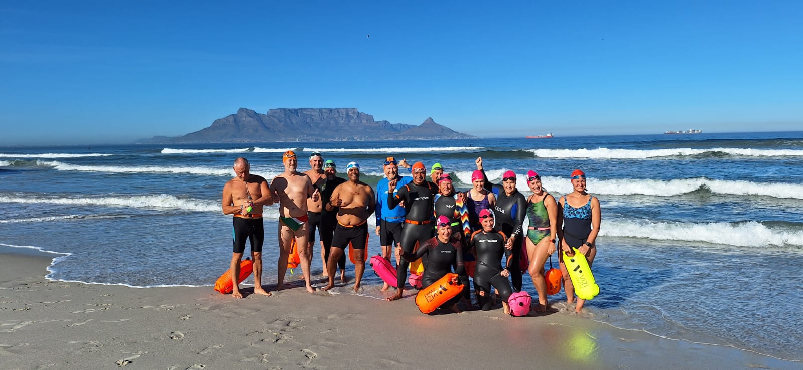 Swimmers posing on the beach with Table Mountain behind them